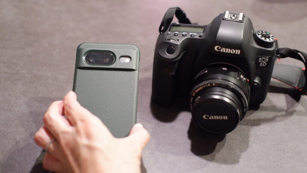 EOS 6Dと小型カメラを机に並べ、手に小型カメラを持って大きさを比較する構図
